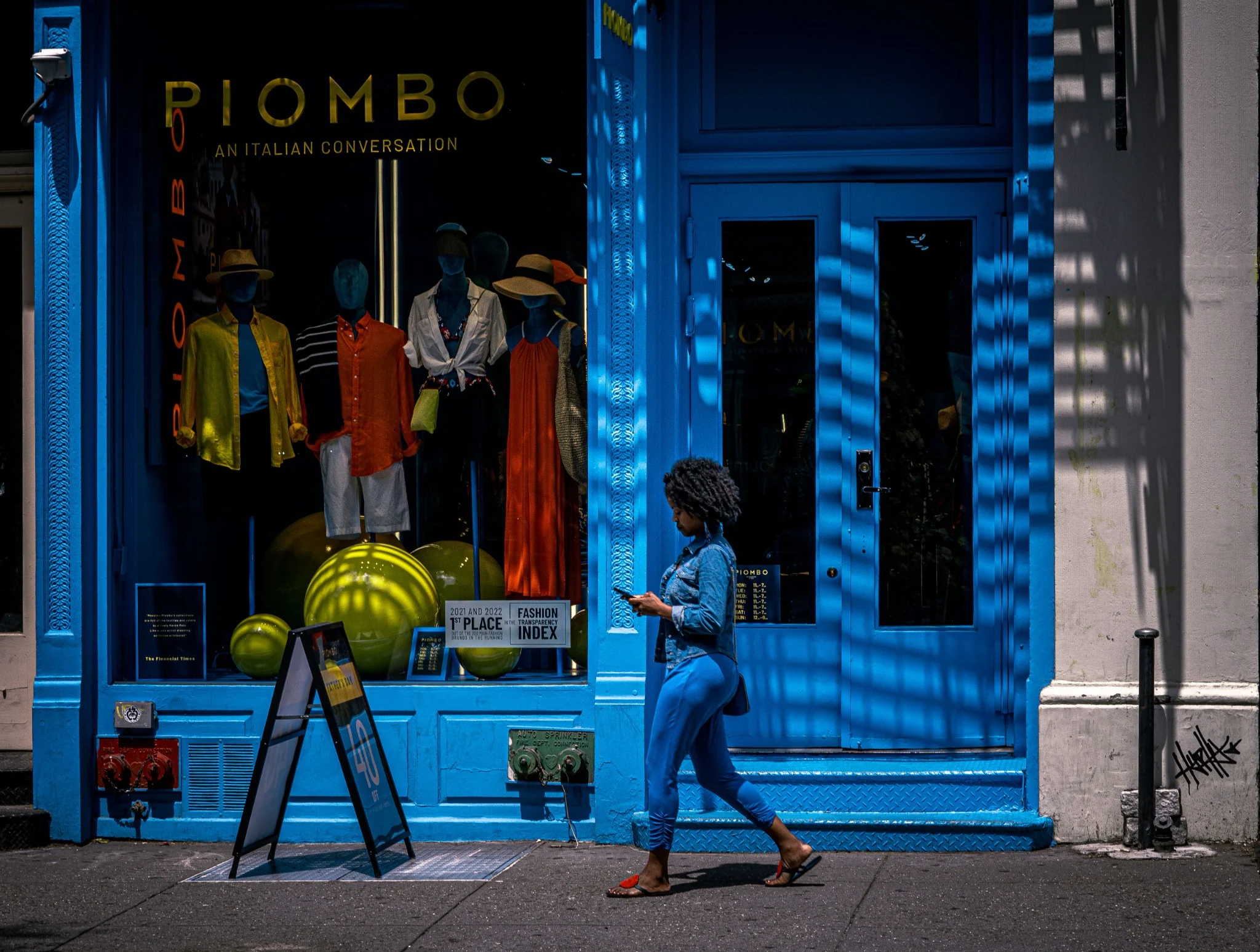 A woman using a phone while walking past a storefront.