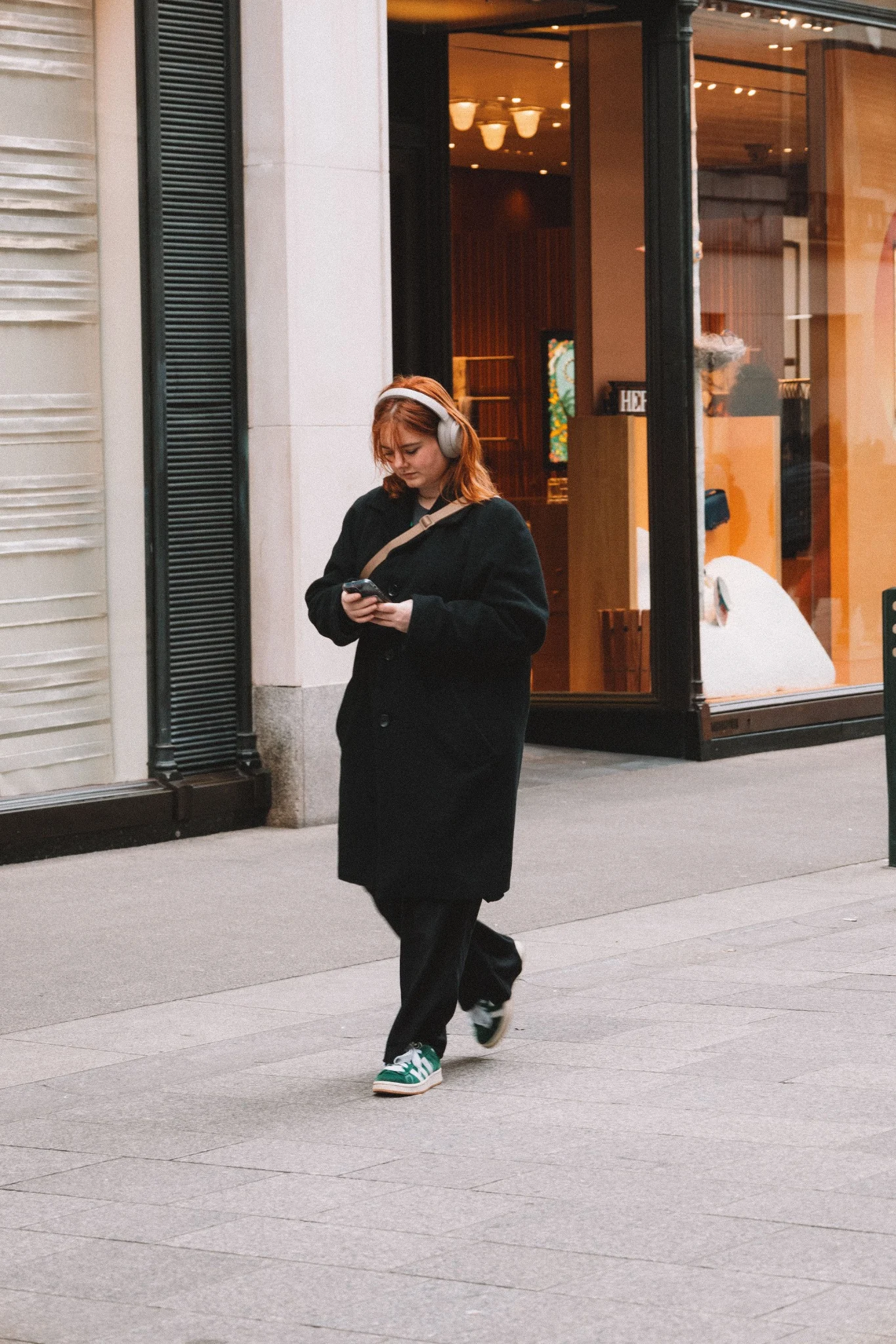 A person using a phone outside a storefront in a commercial district.